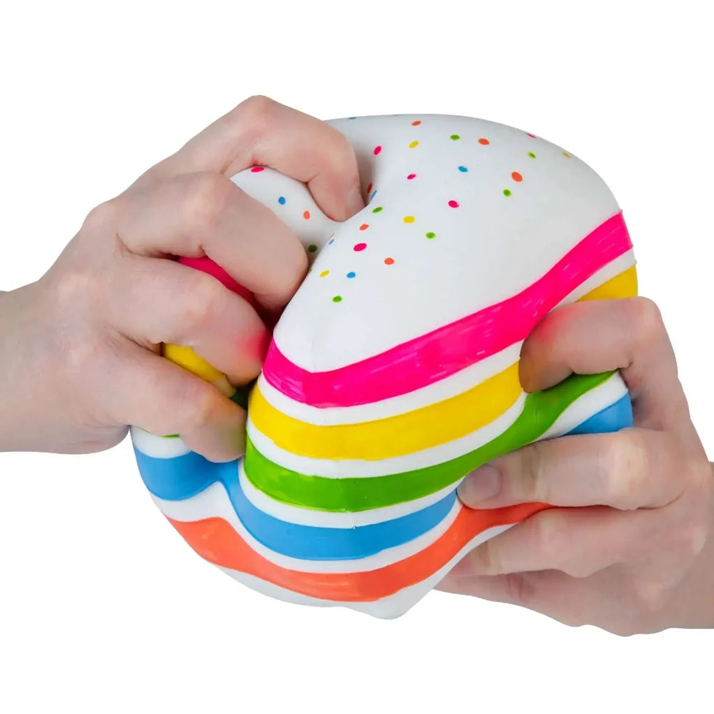 Colorful striped cake squishy toy being squeezed by hands on a white background