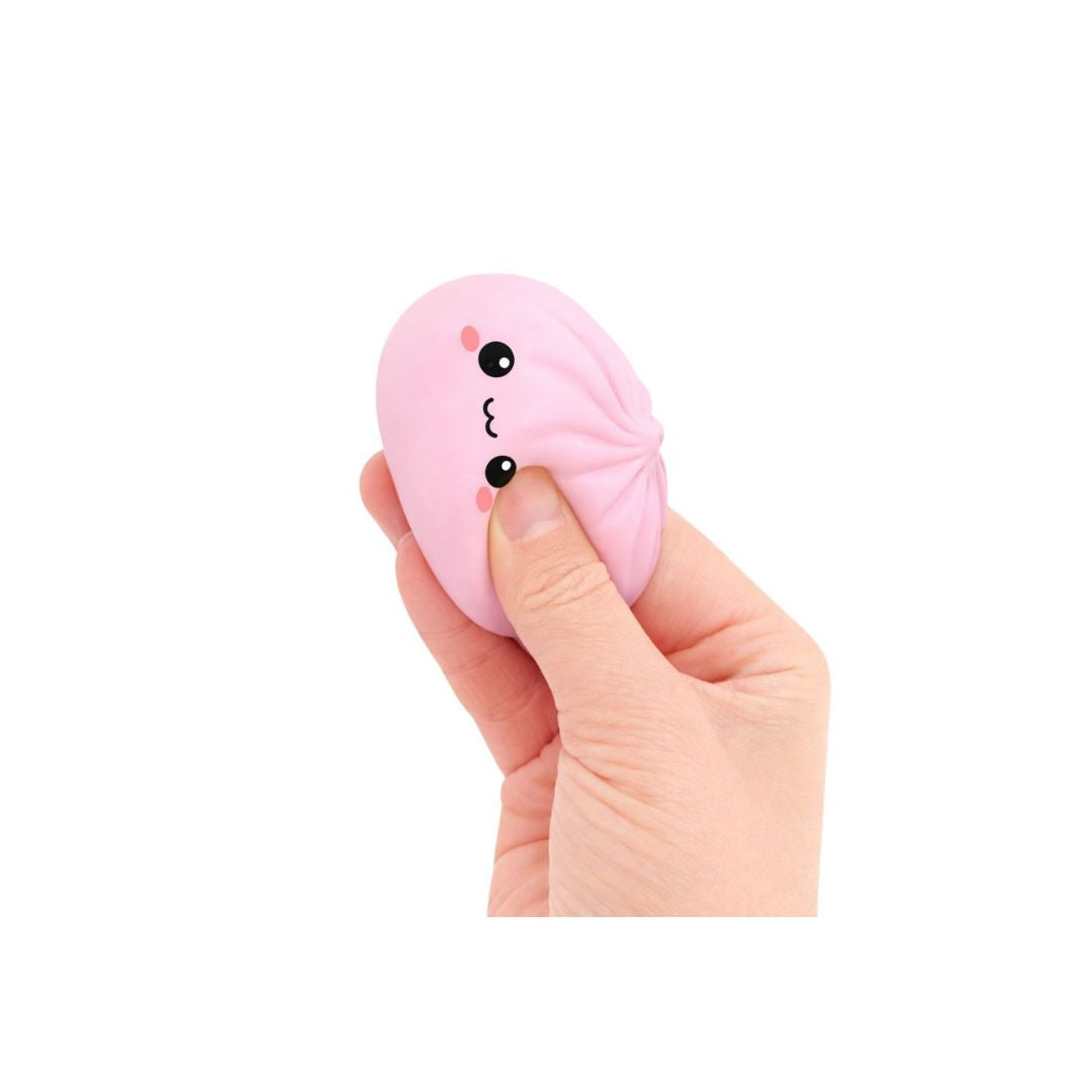 Hand squeezing a pink dumpling‑shaped squishy toy with a small smiling cartoon face, shown against a white background.