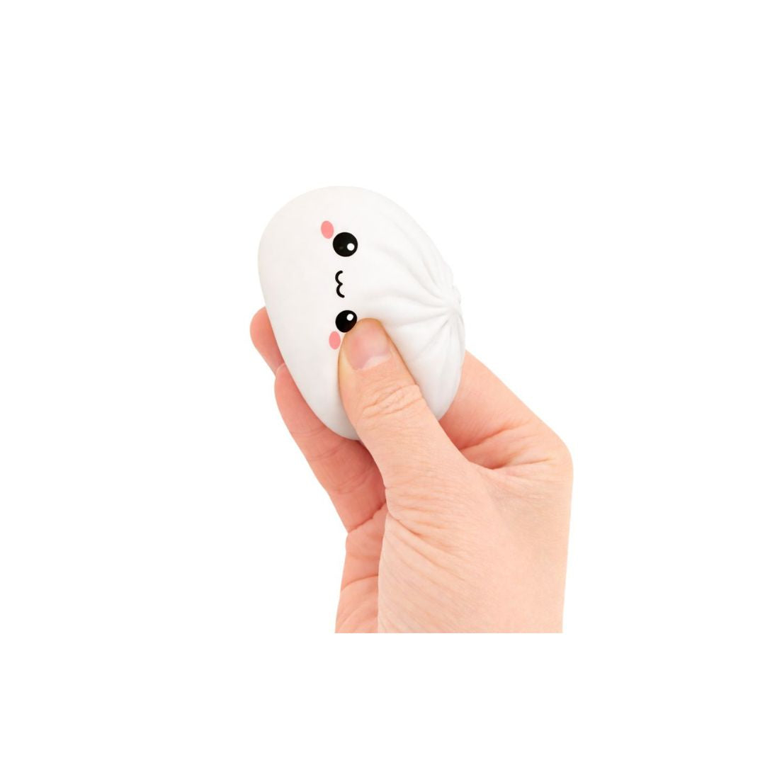 Hand squeezing a small white dumpling‑shaped squishy toy with a smiling cartoon face, shown against a white background.
