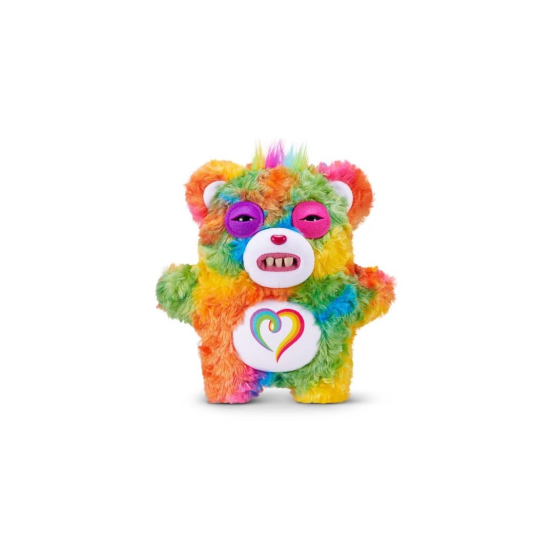 Multicolored tie‑dye Care Bears plush bag charm with a fuzzy textured body, rainbow‑colored fur, a white belly emblem featuring a multicolor heart, pink eyelids, small white teeth, and a short tuft of rainbow hair on top, shown on a white background.