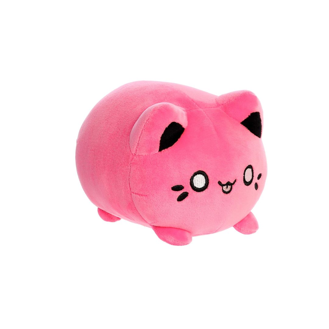 Angled front view of a small pink plush toy shaped like a rounded cat, with black inner ears, embroidered eyes, whisker markings, a small stitched smiling mouth with tongue showing, and short stubby legs, displayed on a white background.