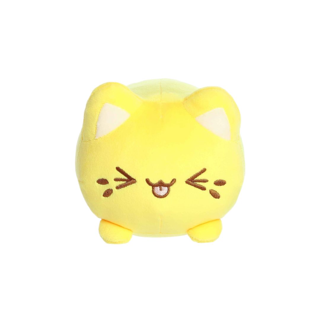 Front view of a small yellow plush toy shaped like a round cat, with white inner ears, embroidered closed eyes, whisker markings, a stitched smiling mouth with tongue showing, and short stubby legs, displayed on a white background.
