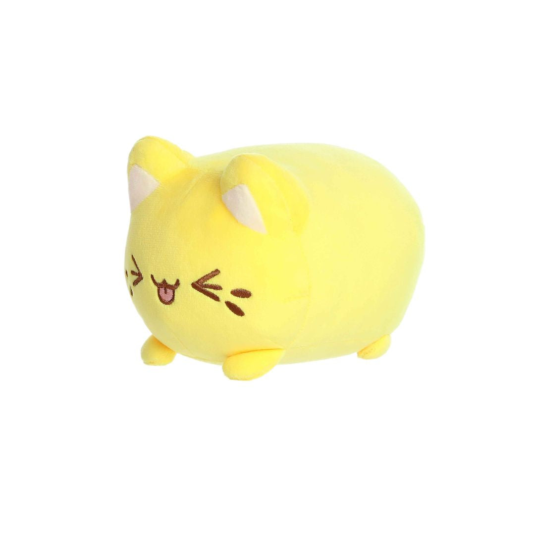 Angled front view of a small yellow plush toy shaped like a rounded cat, with white inner ears, embroidered closed eyes, whisker markings, a stitched smiling mouth with tongue showing, and short stubby legs, displayed on a white background.