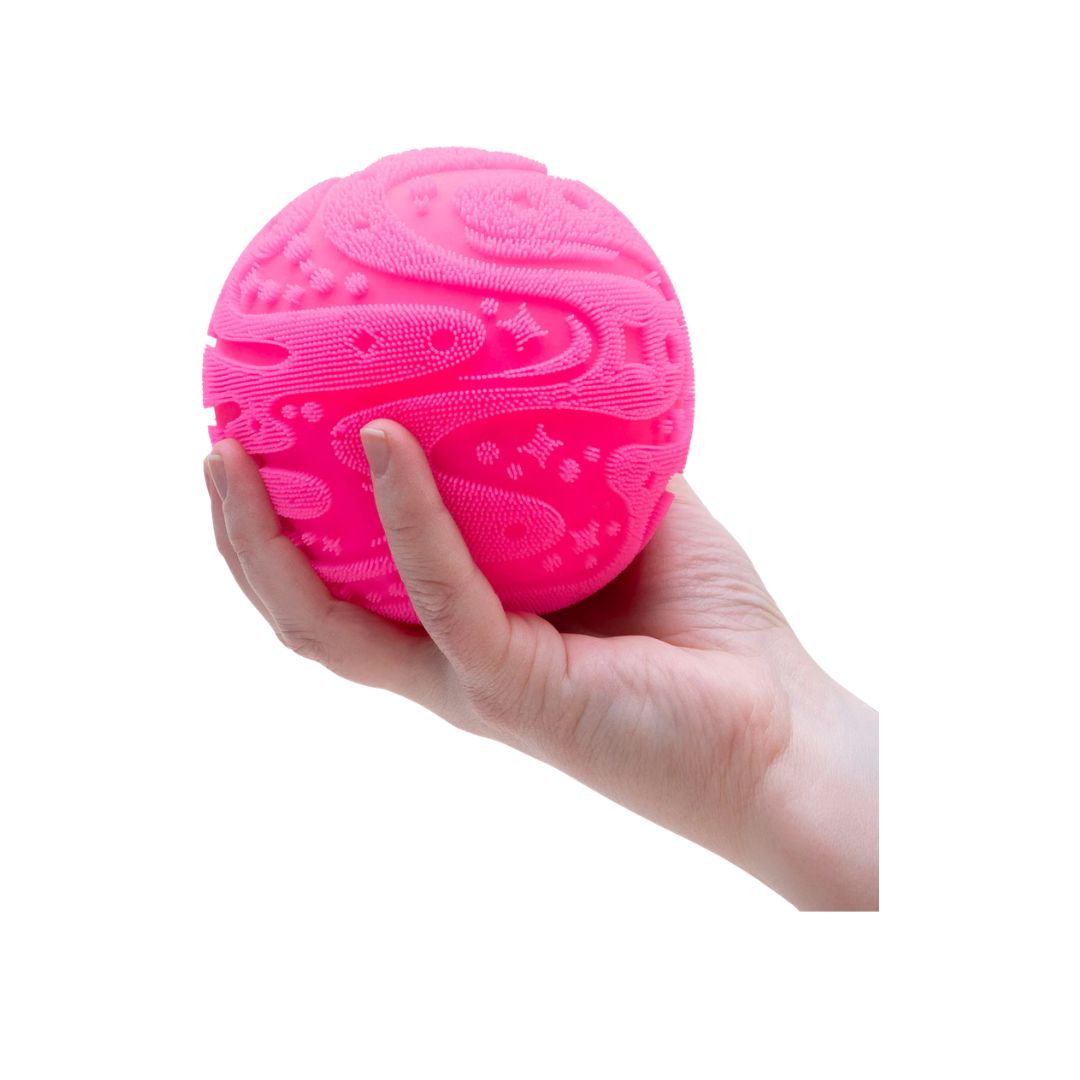Front and side view of a boxed “Super NeeDoh Fuzz Ball” squishy toy, shown in green and black packaging with a circular window revealing a bright green fuzzy ball inside. The box features the text “Super NeeDoh Fuzz Ball” and “The Velvet Squeeze!” with an age rating of 3+.