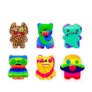 Six colorful, cartoonish monster-shaped accessories arranged in two rows on a plain white background. The items feature vibrant psychedelic patterns including leopard print, blue and purple swirls, rainbow stripes, and multicolor gradients.