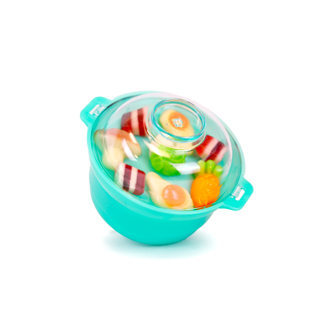 A turquoise hot pot–style container with a clear lid shows food-shaped candies in blue liquid inside, including egg, vegetable, and meat-like pieces.