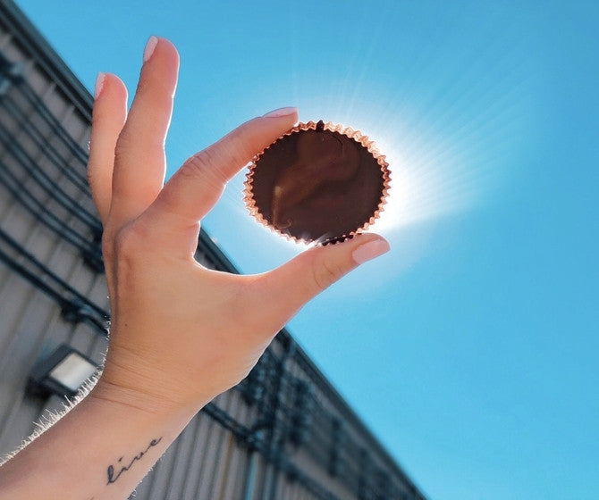 Hand holding a chocolate cup against a bright blue sky