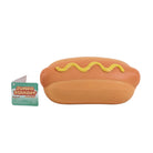 A novelty hot dog squishy toy next to its original packaging card on a white background. The squishy features a tan bun with yellow mustard drizzle, and the packaging card on the left reads 'JUMBO SQUISHY'.