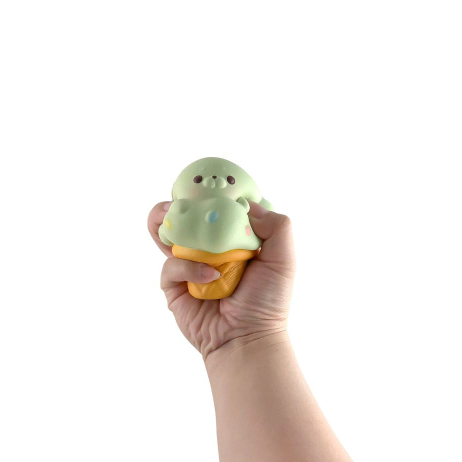 Hand squeezing a green seal ice cream cone–shaped squishy toy against a white background.