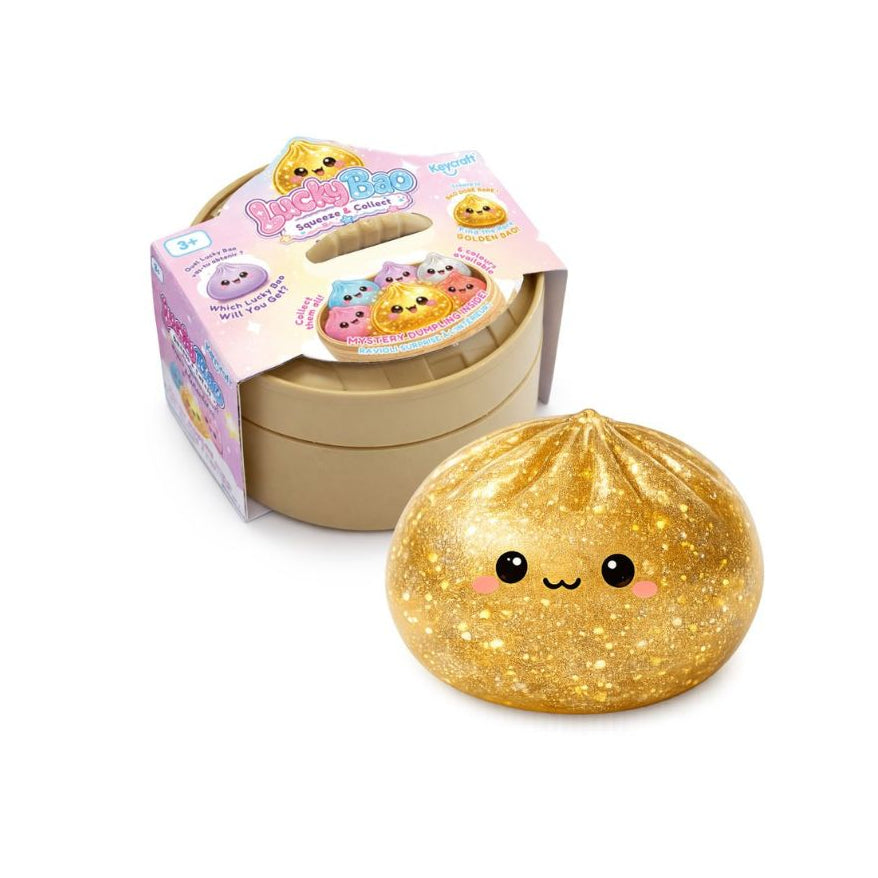 Gold glittery dumpling‑shaped squishy toy with a smiling cartoon face, shown in front of its pastel‑colored product box on a white background.