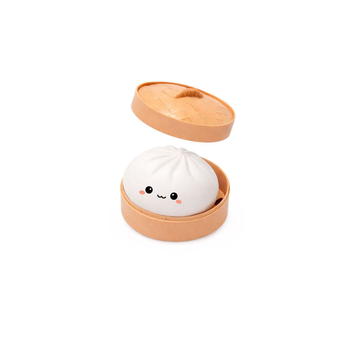 Open round tan container with the lid slightly raised above, holding a white dumpling‑shaped squishy toy with a small smiling cartoon face, shown on a white background.