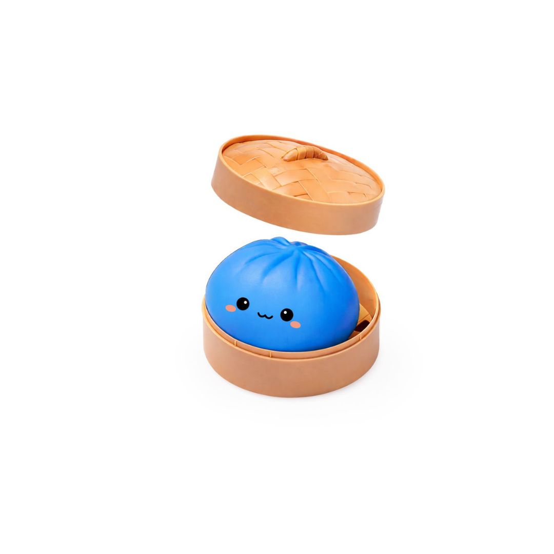 Open round tan container with the lid slightly raised, holding a blue dumpling‑shaped squishy toy with a small smiling cartoon face on a white background.