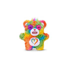 Multicolored tie‑dye Care Bears plush bag charm with a fuzzy textured body, rainbow‑colored fur, a white belly emblem featuring a multicolor heart, pink eyelids, small white teeth, and a short tuft of rainbow hair on top, shown on a white background.