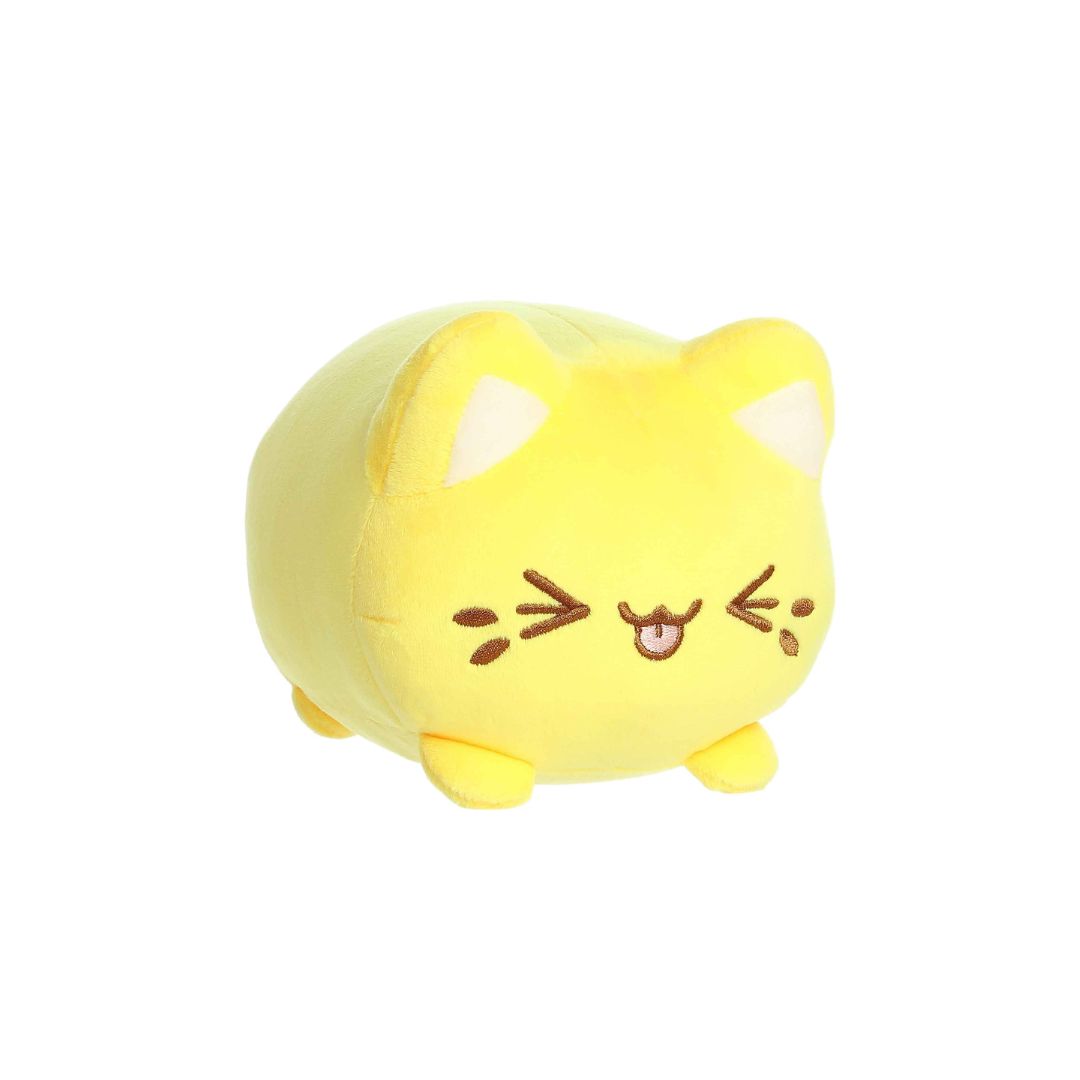 Angled front view of a small yellow plush toy shaped like a round cat, with white inner ears, embroidered closed eyes, whisker markings, a stitched smiling mouth with tongue showing, and short stubby legs, displayed on a white background.