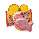 Packaged pink fish‑shaped candy with a yellow filling layer, shown with the wrapper and sweet potato slices on a white background.