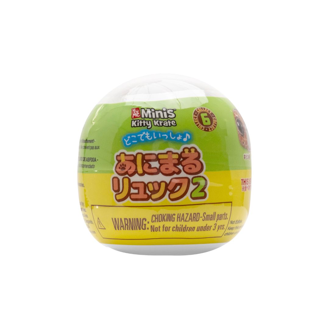 Green and yellow capsule toy labeled ‘Me Minis Kitty Krate’ with Japanese text and a choking hazard warning, shown on a white background.