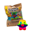 A Fuggler brand 'Mini Squeezables' soft riding stress relief foam piece shown next to its brown cardboard mystery packaging bag on a white background.