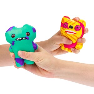 Two hands holding colorful squishy toy fugglers against a plain white background. One toy is teal-green with purple accents, and the other is yellow-orange with pink accents.