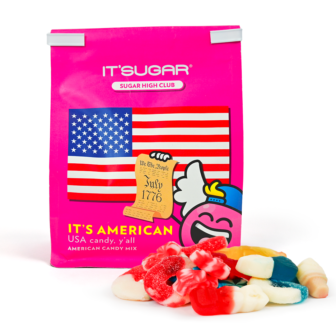 Bright pink IT’SUGAR “IT’S American” candy mix bag featuring an American flag graphic, placed on a white background with assorted red, white, and blue gummy candies in front.