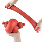 Red Easy Squeezy Sausage toy being squeezed by hands on a white background