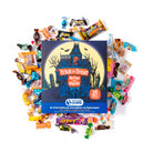 A boxed candy countdown product labeled 'Trick or Treat Across the World!' surrounded by assorted wrapped candies on a white background. The box is dark blue with a haunted-house illustration and a yellow moon, and the brand 'International Yums' is visible on the front.