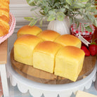 Maison De Pan Hawaiian Roll Squishy toys on a wooden board with a plant and strawberries in the background